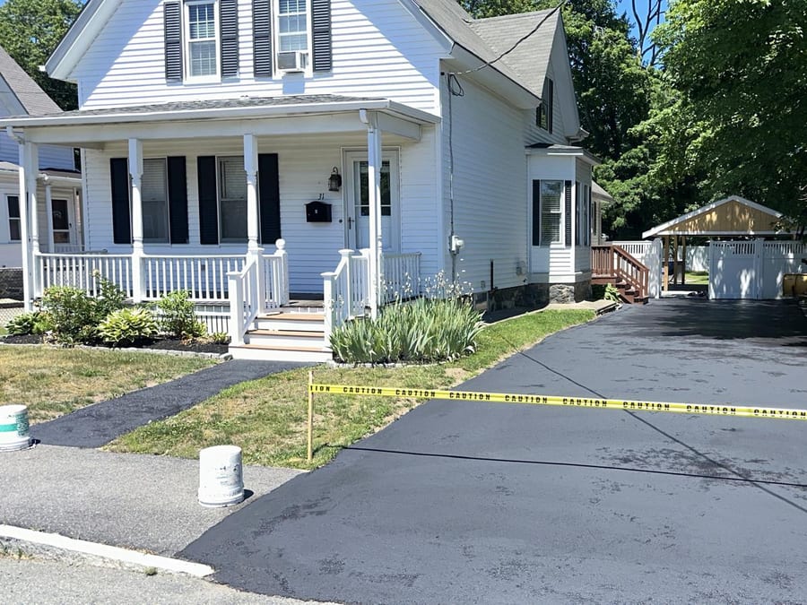 Wide driveway freshly sealed with caution tape across the entrance