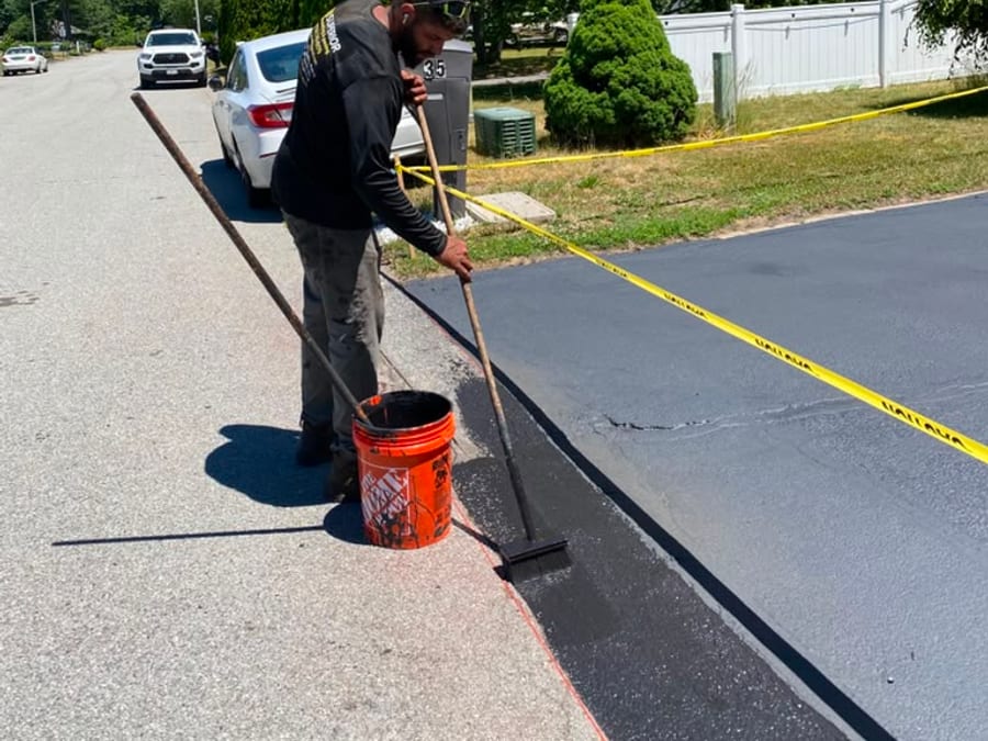 Worker hand applying sealer along the edge of a driveway